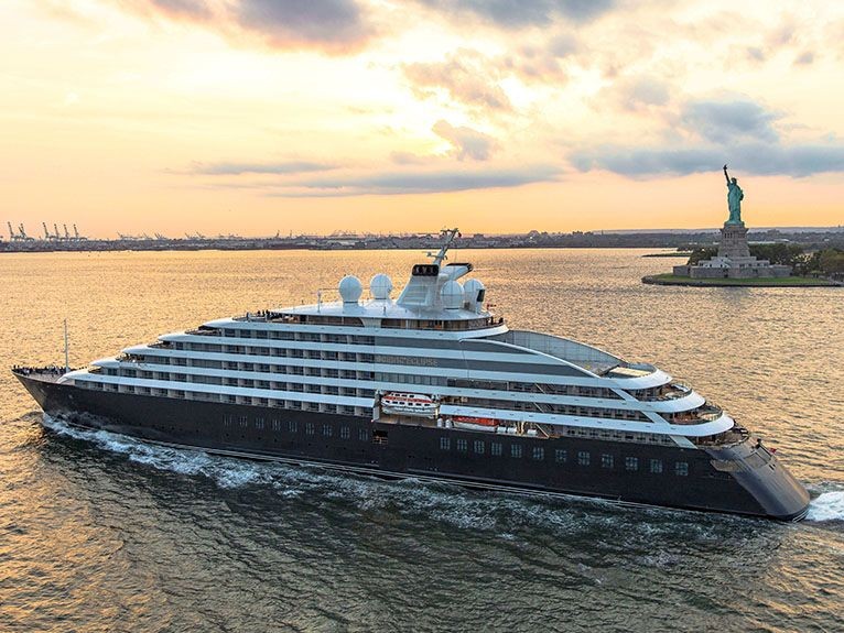 Luxurious cruise ship sailing near the Statue of Liberty during sunset.